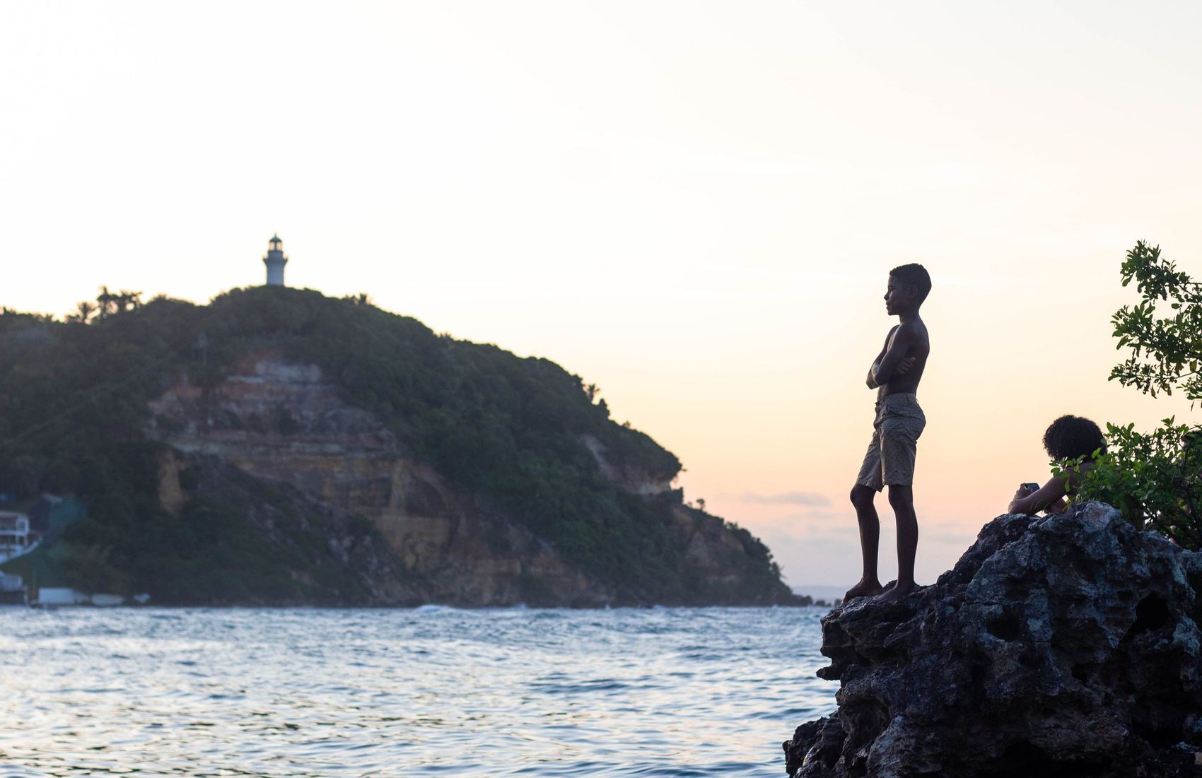 Meninos na beira do costão com farol ao longe